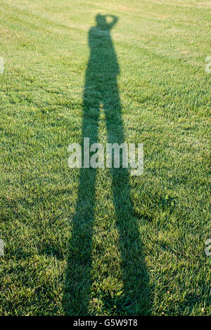 Eine Person wirft lange Schatten auf Rasen Fotos Stockfoto