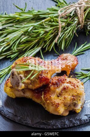 Gebratene Hähnchenschenkel und Rosmarin auf dem schwarzen Hintergrund. Mit Sauce aus Senf, Orange, Honig und Olivenöl zubereitet. Stockfoto