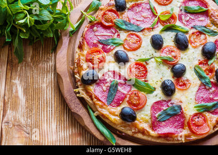 Pizza mit Salami, schwarzen Oliven und Tomaten auf dem Holztisch. Stockfoto