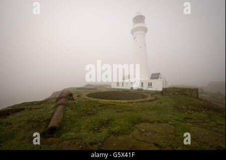 Flat Holm Lighthouse wird durch dichten Nebel mit einem der alten viktorianischen Geschützstellungen im Vordergrund gesehen, komplett mit Moncrieff Grube, aus Kalksteinblöcken und Ziegeln gebaut, die eine geflüchtete 7-Zoll-7-Tonnen-Kanone untergebracht hätte. Stockfoto