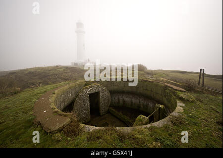 Flat Holm Lighthouse wird durch dichten Nebel mit einem der alten viktorianischen Geschützstellungen im Vordergrund gesehen, komplett mit Moncrieff Grube, aus Kalksteinblöcken und Ziegeln gebaut, die eine geflüchtete 7-Zoll-7-Tonnen-Kanone untergebracht hätte. Stockfoto