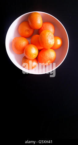 Mandarinen in einer weißen Schüssel auf schwarzem Hintergrund Stockfoto