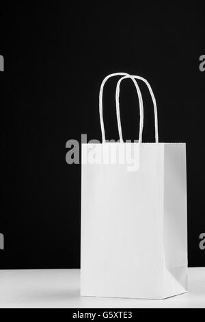 Leeres weißes Papier Tasche mit Griffen auf weiße Theke mit schwarzem Hintergrund und Schatten. Stockfoto