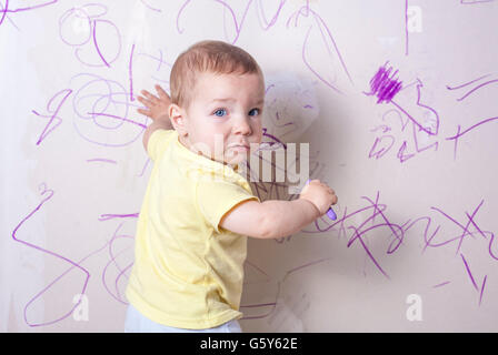 Baby Junge Gipskartonwand mit Wachs Buntstift schöpfend. Er blickt in die Kamera Stockfoto