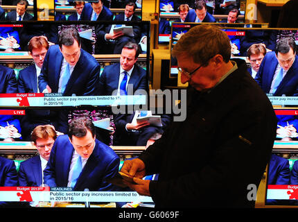 Ein Mann schaut auf seine Brieftasche, während Schatzkanzler George Osborne während der Budgetankündigung in einem John Lewis-Laden, Solihull, West Midlands, auf Fernsehbildschirmen zu sehen ist. Stockfoto