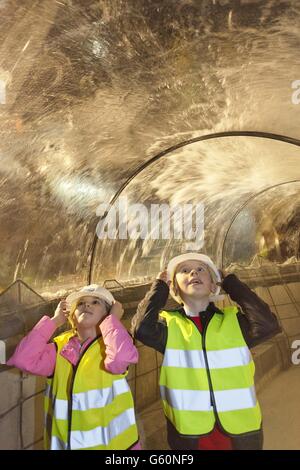 Aimee Johnstone im Alter von 8 und Declan Whitmore im Alter von 9 Jahren von der Knowsley Junior Schoolstand in einem Tunnel in Sea Life Manchester im Trafford Centre, während das Regenwasser, das sie gesammelt haben, die Tanks des Aquariums füllt, um sich auf einige Neuankömmlinge im nächsten Monat vorzubereiten. Stockfoto