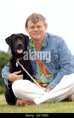 Schauspieler Martin Clunes, die Stimme des Zeichentrickfilm-Hundes „Merlin“ im Fernsehen, mit einem acht Monate alten Blindenhund, der auch Merlin genannt wird, der im Ausbildungszentrum der Blindenvereinigung in Woodford, Essex, Guide Dogs ausgebildet wird. Stockfoto