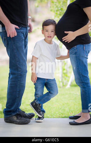 Neugierigen jungen gemischt Rennen Sohn mit Ohr am Bauch von Mama mit Papa in der Nähe. Stockfoto