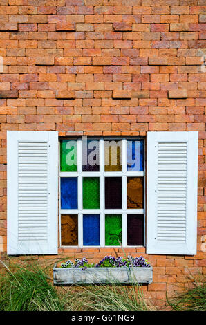 Weiße Fenster und buntes Glas auf orange Ziegelwand Stockfoto