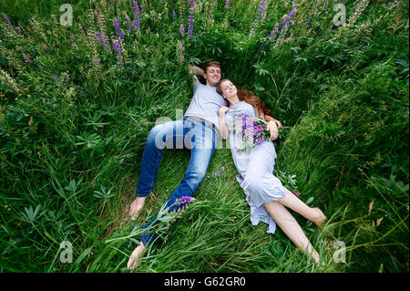 Mann und Frau umarmen, Gras auf einer Wiese mit Bouquet von Lupinen liegend Stockfoto