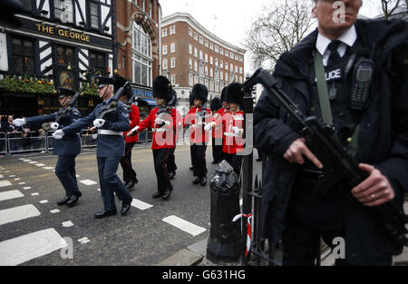 Ein bewaffneter Polizeibeamter steht Wache, während Militärpersonal vor der feierlichen Trauerprozession von Baroness Thatcher in der St. Paul's Cathedral im Zentrum von London vorbeimarschieren muss. Stockfoto