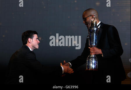 Der Gareth Bale von Tottenham Hotspur schüttelt mit dem PFA-Vorsitzenden Clarke Carlisle die Hände, während er auf die Bühne geht, um seinen PFA Player of the Year Award während der PFA Player of the Year Awards 2013 im Grosvenor House Hotel in London zu sammeln. Stockfoto