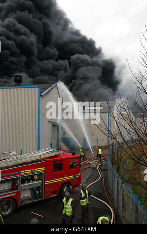 Am ersten Tag des achttägigen Streiks der nationalen Feuerwehrleute ergiebt sich schwarzer Rauch aus einer stillgetrauten Kunststofffabrik in West Bromwich, als Soldaten mit einem roten Feuerwehrmotor dort einen massiven Brand bekämpfen. * streikende Feuerwehrleute der nahe gelegenen Basis Willenhall brachen auch ihre Streikposten, um an der Szene teilzunehmen. Stockfoto