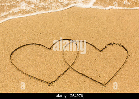 Zwei Herzen auf den Strandsand gezeichnet. Stockfoto