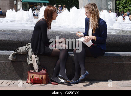 Büroangestellte genießen die Sonne, als die Temperaturen auf 19c in Canary Wharf in London stiegen. Stockfoto