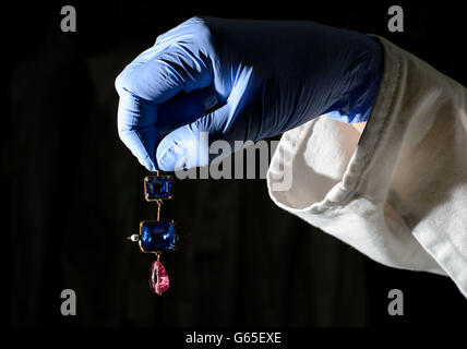 Ein Konservator hält einen Anhänger aus Gold und Emaille, der mit zwei Saphiren verziert ist, die Teil des Cheapside Horths sind, der weltweit größten Sammlung von Schmuck aus dem Elisabethanischen und frühen Stuart, an einer Fotoausstellung im Museum of London im Zentrum Londons. Stockfoto