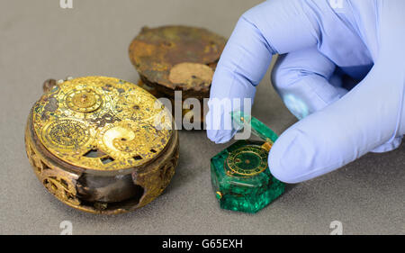 Ein Konservator öffnet den Deckel einer kolumbianischen Smaragd-Uhr, die neben einer Gilde aus Messing, Teil des Cheapside Hoard, der weltweit größten Sammlung von elisabethanischen und frühen Stuart Schmuck, bei einer Fotoausstellung im Museum of London im Zentrum von London zu sehen ist. Stockfoto