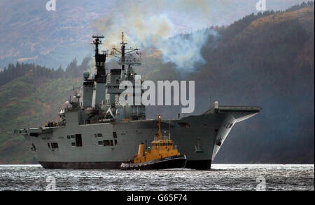 Der britische Flugzeugträger HMS Ark Royal wird von einem Schleppboot auf Loch Long begleitet, als er zum Standort Glen Douglas in Schottland auffährt. Die Arche Royal wird dort Geschäfte machen, bevor sie sich auf einen Einsatz begibt, der sie ins Mittelmeer und möglicherweise in den Golf führen wird. * 16/1/03: Das mächtigste Kriegsschiff Großbritanniens sollte von Schottland aus in See stechen, nachdem es seine letzten Vorbereitungen für einen möglichen Krieg im Golf abgeschlossen hatte. HMS Ark Royal sollte die Waffenbasis Glen Douglas am Ufer des Loch Long, Argyll, verlassen und in Richtung Mittelmeer fahren, wo sie teilnehmen wird Stockfoto