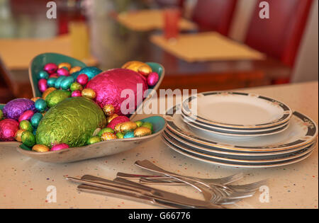 Zeit der Osterfeier.  Farbige bunte Schokolade Ostereier in einer Schüssel neben einem Esstisch set für eine Party. Stockfoto
