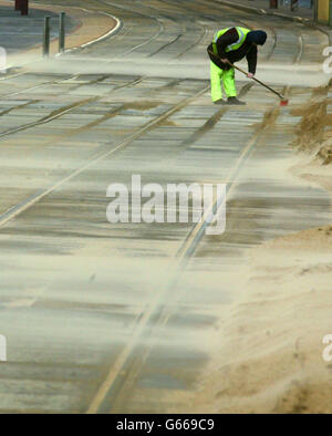 Ein einmütiger Arbeiter kämpft darum, die Straßenbahnschienen an der Küste von Blackpool frei zu halten, da starke Winde einen Großteil der Promenade im Sand bedecken. Stockfoto