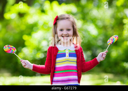 Niedliche kleine Mädchen mit großen bunten Lollipop. Kind, essen Süßigkeiten Bar. Süßigkeiten für kleine Kinder Stockfoto