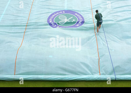 Ein Platzwart arbeitet zu Beginn des fünften Tages der Wimbledon Championships im All England Lawn Tennis and Croquet Club, Wimbledon, daran, die Abdeckung des Platzes zu entfernen. Stockfoto