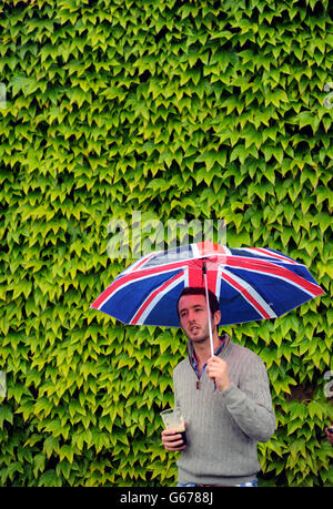 Tennis - Wimbledon Championships 2013 - Tag fünf - All England Lawn Tennis und Croquet Club. Ein Ventilator schützt vor dem Regen unter seinem britischen Flaggen-Schirm Stockfoto