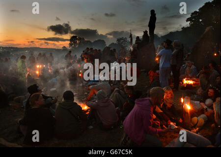 Festivalbesucher entspannen sich am Steinkreis, wenn die Sonne nach dem letzten Tag des Glastonbury 2013 Festivals auf der Pilton Farm, Somerset, aufgeht Stockfoto