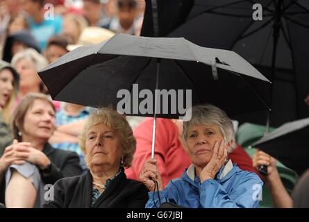 Am vierten Tag der Wimbledon Championships im All England Lawn Tennis und Croquet Club in Wimbledon schützen Fans sich mit einem Regenschirm vor dem leichten Regen. Stockfoto