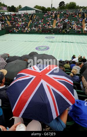 Am vierten Tag der Wimbledon Championships am All England Lawn Tennis und Croquet Club in Wimbledon schützen sich Fans vor dem Regen auf dem Platz zwei. Stockfoto