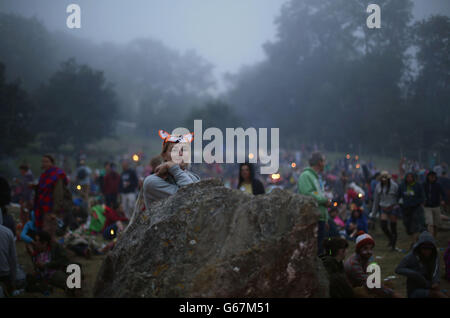 Festival-Besucher warten auf Sonnenaufgang am Stone Circle, beim Glastonbury Festival, Worthy Farm in Somerset. Stockfoto