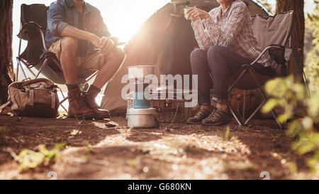 Bild von Mann und Frau sitzen auf Stühlen außerhalb des Zeltes zugeschnitten. Paar camping im Wald. Stockfoto