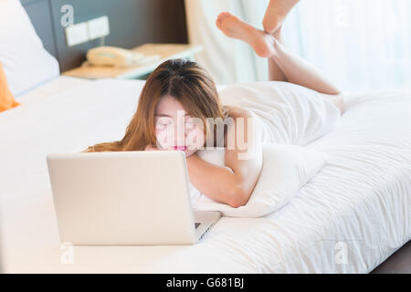 Schöne junge Frau im Bademantel eingeschlafen während mit Laptop im Bett zu Hause Stockfoto