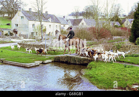 Ein Jäger der Heythrop-Fuchsjagd an den Grenzen von Oxfordshire, Warwickshire und Gloucestershire führt sein Jagdhundrudel über einen Steg im Dorf Upper Slaughter. * The League Against Cruel Sports stellte heute Videomaterial vor, in dem ein ehemaliges Mitglied der Heythrop Hunt Hunde in eine der künstlichen Fuchserden ließ. 30/6/03: Die Abgeordneten diskutieren über ein umstrittenes neues Gesetz, das es ermöglichen würde, die Fuchsjagd fortzusetzen, aber unter einem strengen Regulierungssystem. Während Hasen-Coursing und Hirschjagd nach den vorgeschlagenen Rechtsvorschriften verboten werden würden, wollen eine große Anzahl von Abgeordneten Fuchsjagd Stockfoto