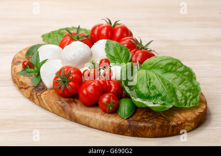 Italienische Küche. Mozzarella, Heirloom Tomaten, Basilikum-Blätter auf einem hölzernen Teller. Selektiven Fokus auf Käse Stockfoto