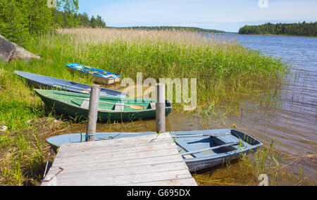 Kleine Ruderboote lag an der Küste noch See in der Nähe von hölzernen pier Stockfoto