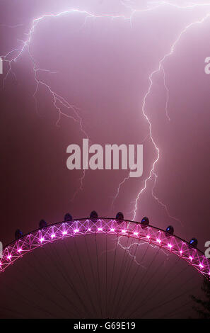 Hinter dem London Eye im Zentrum Londons, das zur Geburt eines kleinen Jungen um 16.24 Uhr an den Herzog und die Herzogin von Cambridge im St. Mary's Hospital in den Farben Rot, Weiß und Blau gehalten ist, schlägt ein Blitz ein. Stockfoto