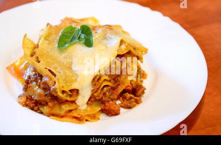 Hausgemachte gekochte Lasagne Bolognese mit Basilikum Blätter auf weißen Teller. Stockfoto