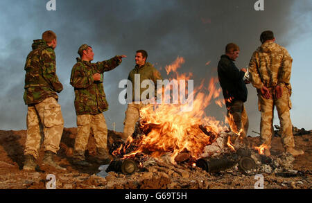 Britische Soldaten von 29 Commando Regiment Royal Artillery versammeln sich um ein Feuer in der Morgendämmerung nach einer geschäftigen Nacht auf der Schusslinie, als der Himmel hinter wird durch ein Ölfeuer am Horizont im Südirak geschwärzt. Mit dem Eintritt des Irak-Konflikts in die zweite Woche. Stockfoto