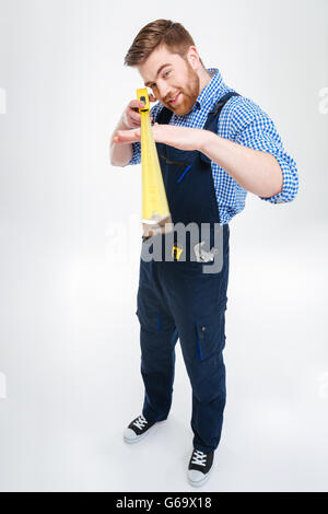 Hübscher fokussierte junger Mann Arbeiter stehend und mit Maßband Stockfoto