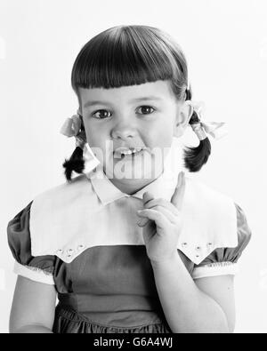 1950ER JAHRE PORTRAIT LÄCHELND MÄDCHEN HAARE IN ZÖPFEN FINGERZEIG BLICK IN DIE KAMERA Stockfoto