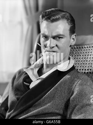 1930S 1940S UNGLÜCKLICHER MENSCH SITZEN HOLDING THERMOMETER IM MUND TRAGEN ROBE SCHLAFANZUG Stockfoto