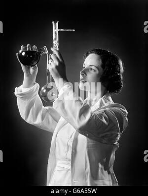 1930ER JAHREN WEIBLICHEN CHEMIKER WISSENSCHAFTLER GIEßEN FLÜSSIGKEIT IN EIN BECHERGLAS Stockfoto