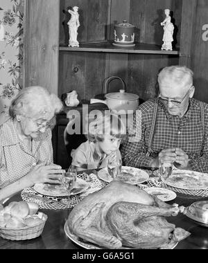 1950ER JAHRE FAMILIE THANKSGIVING DINNER BETEN MÄDCHEN UND GROßELTERN Stockfoto