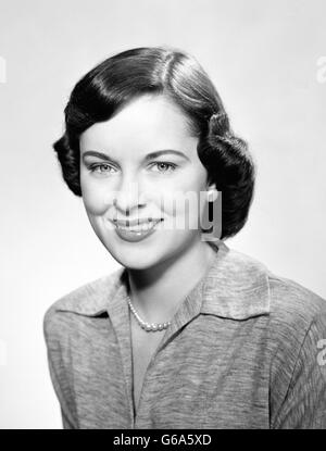 1950ER JAHRE PORTRAIT LÄCHELND BRÜNETTE FRAU MIT BOY FRISUR TRAGEN WÄHLZEICHENFOLGE PERLEN BLICK IN DIE KAMERA Stockfoto