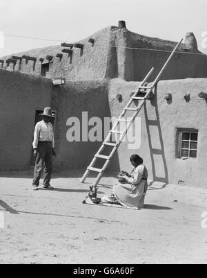 1930ER JAHREN INDIANISCHE PAAR VON ADOBE GEBÄUDE FRAU POLIEREN KERAMIK MANN BLICK AUF SANTA CLARA PUEBLO NEW MEXICO USA Stockfoto