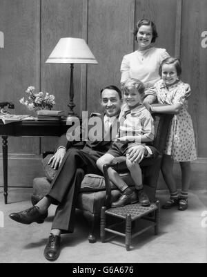 1930ER JAHRE PORTRAIT LÄCHELND FAMILIE VATER MUTTER ZWEI KINDER IM WOHNZIMMER MIT BLICK IN DIE KAMERA Stockfoto