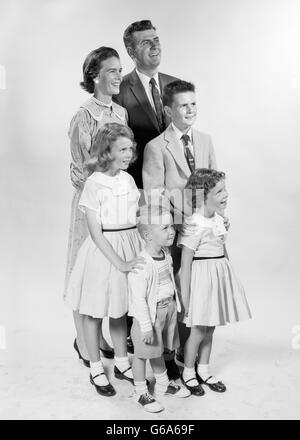 1950ER JAHRE PORTRAIT LÄCHELND FAMILIE 6 MUTTER VATER JUNGEN MÄDCHEN STEHEND Stockfoto