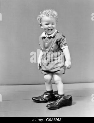 1930S 1940S UNTER DER LEITUNG LAUGHUNG LOCKIGEN BLONDEN JUNGEN ERWACHSENEN SCHUHE VATERS FUßSTAPFEN WANDERBARES Stockfoto