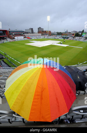 Die Fans halten sich unter Regenschirmen auf, während am fünften Tag des dritten Investec Ashes Testspiels im Old Trafford Cricket Ground, Manchester, der Regen aufhört zu spielen. Stockfoto